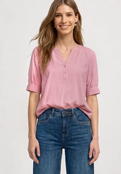 Blouse met korte mouwen, split in de hals en elastische zoom vintage blush Frau in rosa Bluse mit V-Ausschnitt und blauen Jeans, stehend mit Händen an den Seiten.