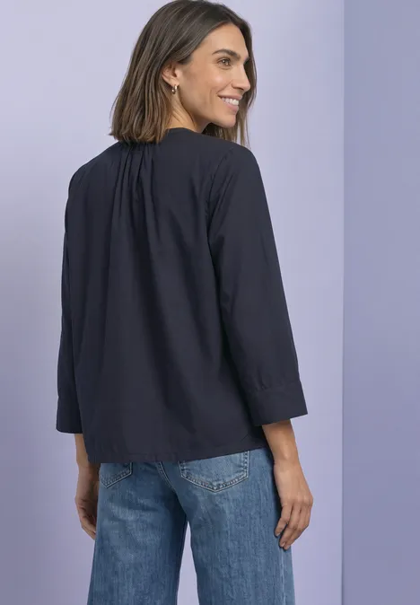 Frau von hinten mit dunkelblauer Bluse und Jeans, blickt über die Schulter vor lilafarbenem Hintergrund.