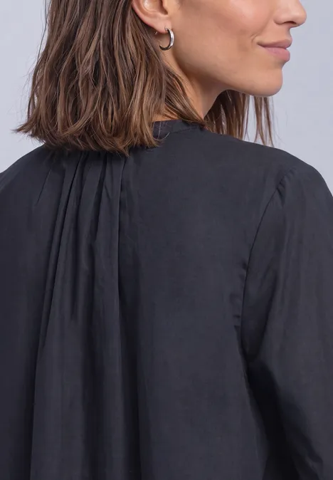 Frau mit schulterlangen braunen Haaren und silbernen Creolen, trägt eine schwarze Bluse, im Profil von hinten.