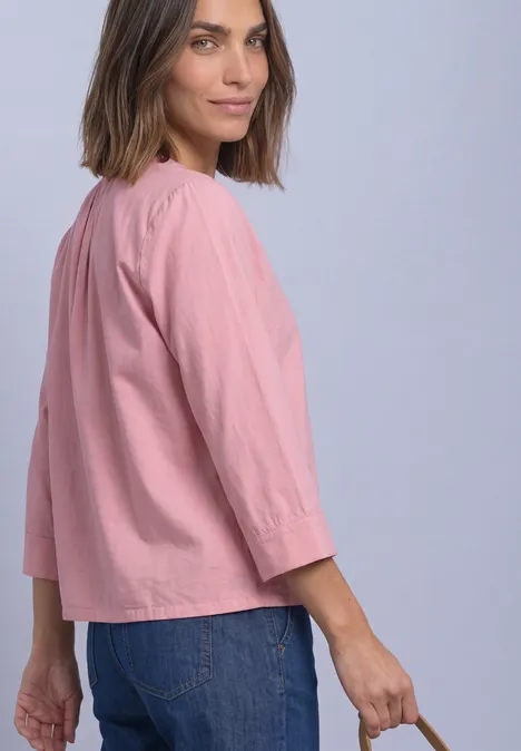 Chemisier à manches 3/4 et col fendu, en velours côtelé vintage blush Frau trägt locker sitzende rosa Bluse mit 3/4-Ärmeln und blaue Jeans, Blick über die Schulter.