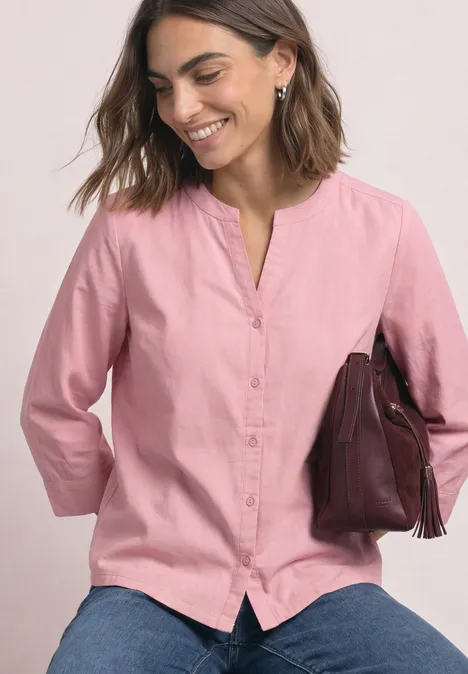 3/4-Arm Bluse mit Split Neck aus Cord vintage blush Frau in rosa Bluse und Jeans, hält braune Handtasche und lächelt freundlich.