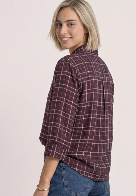 Eine Frau dreht sich über die Schulter, trägt karierte Bluse und Jeans, lächelt.