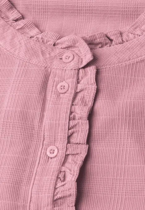 Detailaufnahme einer rosa, strukturierten Bluse mit Rüschenbesatz und Knopfleiste.
