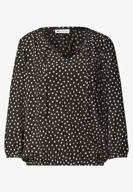 Schwarze Bluse mit weißem Herzpunkte-Muster, V-Ausschnitt und langen Ärmeln.