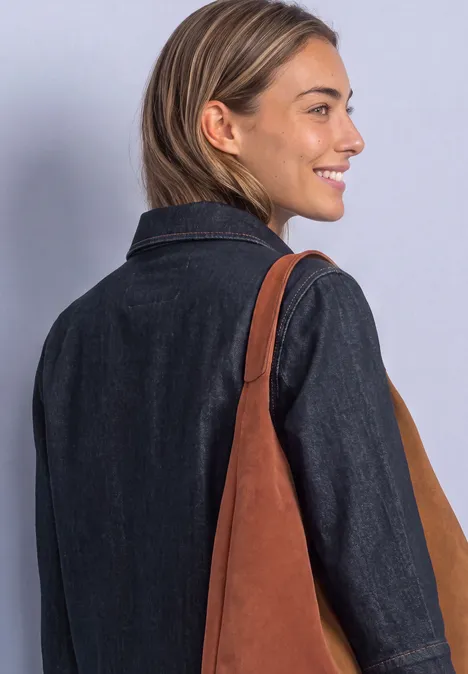 Eine lächelnde Frau im Jeansblazer trägt eine braune Schultertasche.
