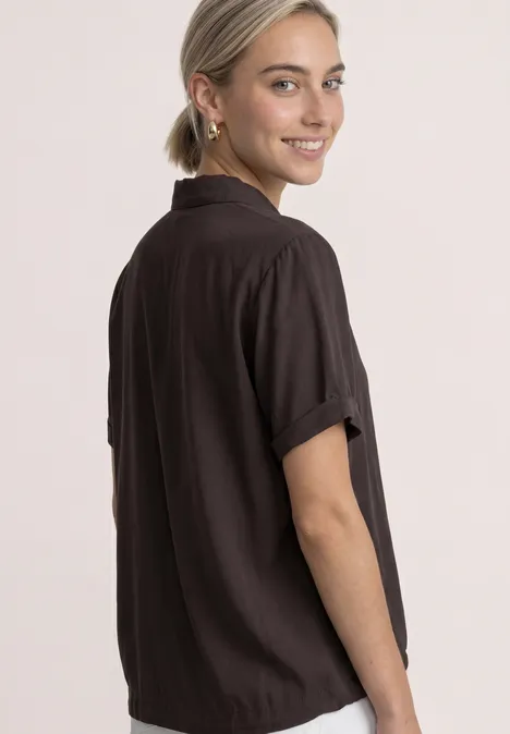 Overhemd met korte mouwen in effen kleur black coffee Lachende vrouw in zwart kort mouw shirt, staand zijwaarts, die over haar schouder kijkt.