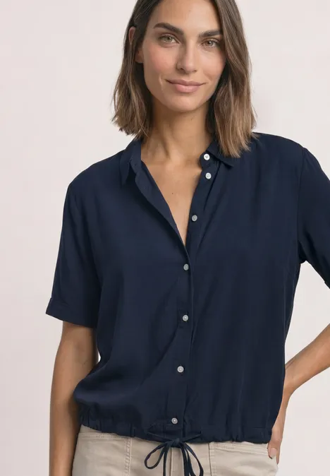 Une femme portant un chemisier bleu marine à manches courtes, taille cintrée et boutons sur le devant.