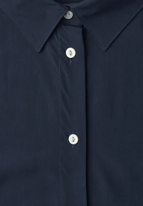 Gros plan sur une chemise bleu marine à boutons blancs et patte de boutonnage cachée.