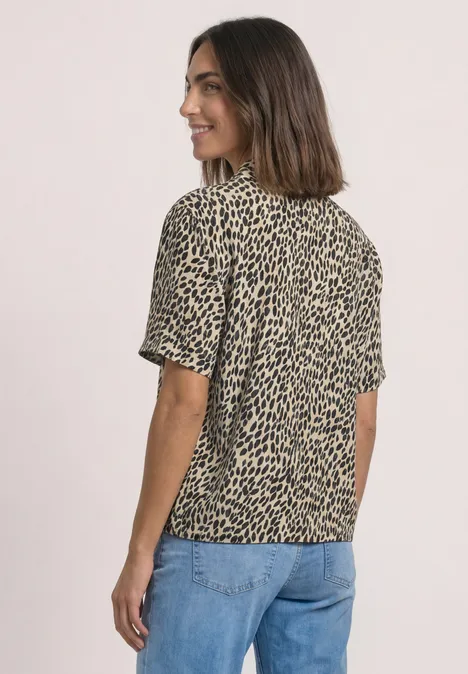Overhemd met korte mouwen en print cotton beige Frau mit beigeschwarzer, kurzärmliger Leo-Bluse und blauer Jeans, seitlich lächelnd.