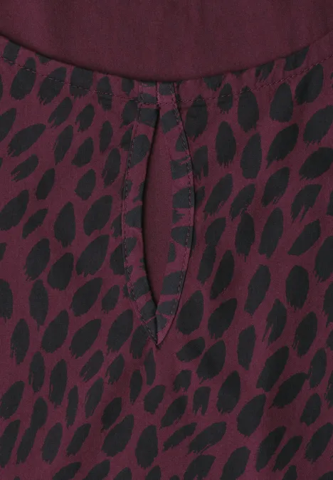 Blouse en tissu bordeaux à motif de feuilles noires avec une petite fente en forme de goutte au col