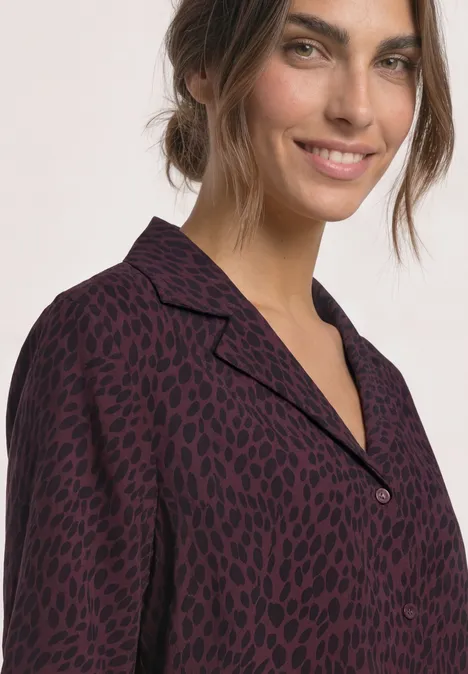 Eine lächelnde Frau trägt eine dunkelrote, schwarz gepunktete Bluse mit Hemdkragen.
