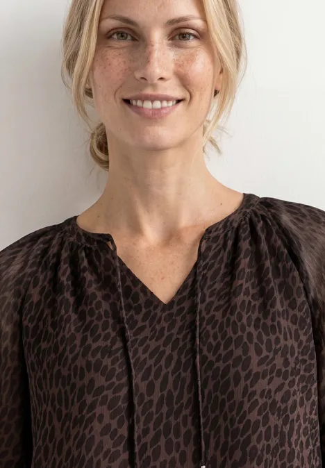 Raglanbluse mit Split Neck und Print molten earth Eine lächelnde Frau in brauner, gemusterter Bluse vor hellem Hintergrund.