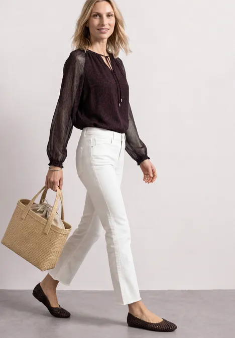 Raglanblouse met split in de hals en print rustic rouge Vrouw in witte broek en zwarte blouse, met beige tas en zwarte loafers.
