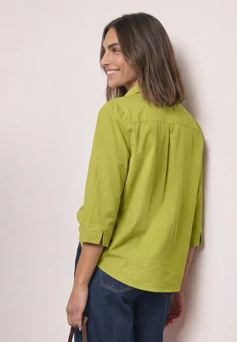 Chemisier à manches 3/4 en mélange de velours côtelé apple lime Frau mit schulterlangem braunem Haar in grüner Bluse und Jeans, seitlich stehend und lächelnd.