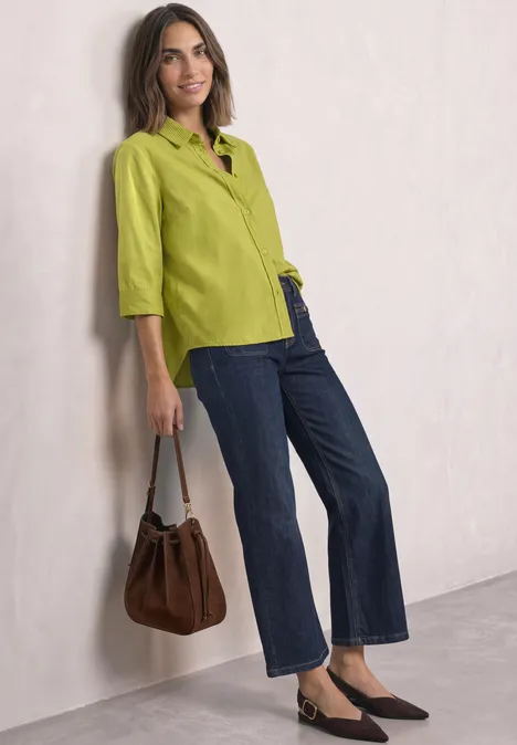 Chemisier à manches 3/4 en mélange de velours côtelé apple lime Frau in grüner Bluse und Jeans, braune Tasche, lässig an Wand gelehnt.