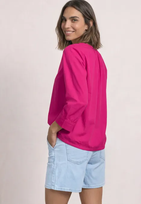 Femme en haut rose et short en jean clair, souriante, regardant par-dessus son épaule.