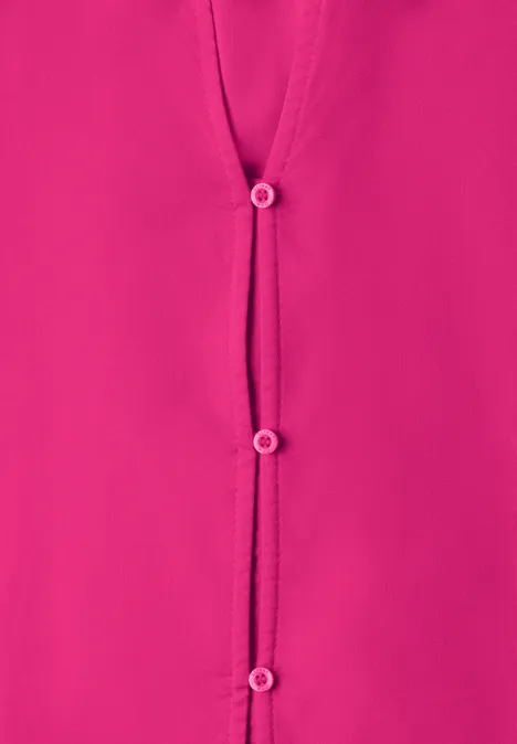 Gros plan sur une blouse rose vif à trois boutons.