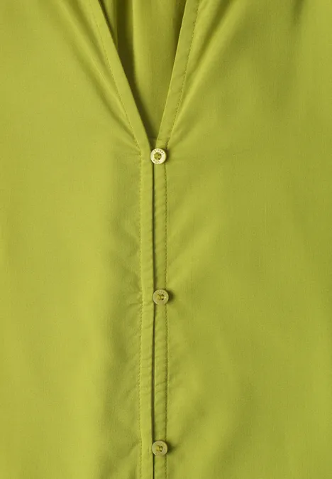 Gros plan sur une chemise vert clair à boutons apparents et coutures visibles.