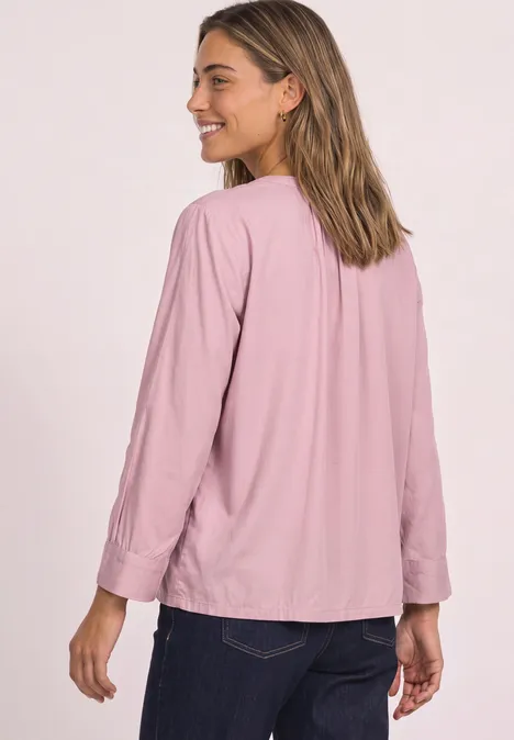 Eine Frau in rosa Bluse und dunklen Jeans blickt lächelnd über die Schulter.