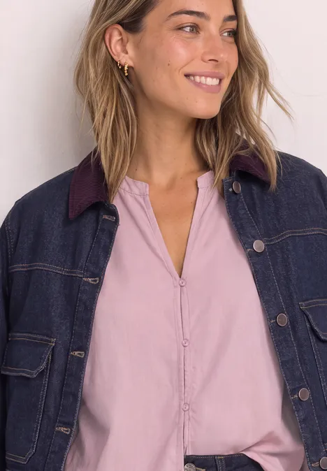 Junge Frau lächelt, trägt ein hellrosa Hemd und eine dunkelblaue Jeansjacke.