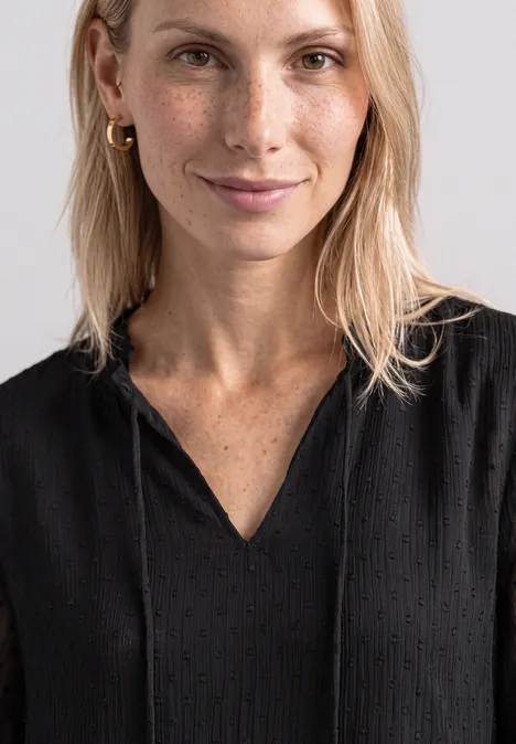 Uśmiechnięta blondynka w czarnej bluzce z piegami na jasnym tle.