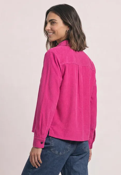 Langarm Cord Hembluse mit Knöpfen magenta dream Frau in pinkem Hemd und blauen Jeans, seitlich stehend, lächelnd.