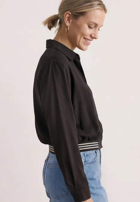 Seitlich abgebildete Frau mit schwarzer Bluse und Jeans, lächelnd.