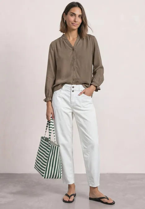 Frau in legerer taupe Bluse, weißen High-Waist-Hosen und schwarzen Sandalen trägt grün-weiß gestreifte Tasche.