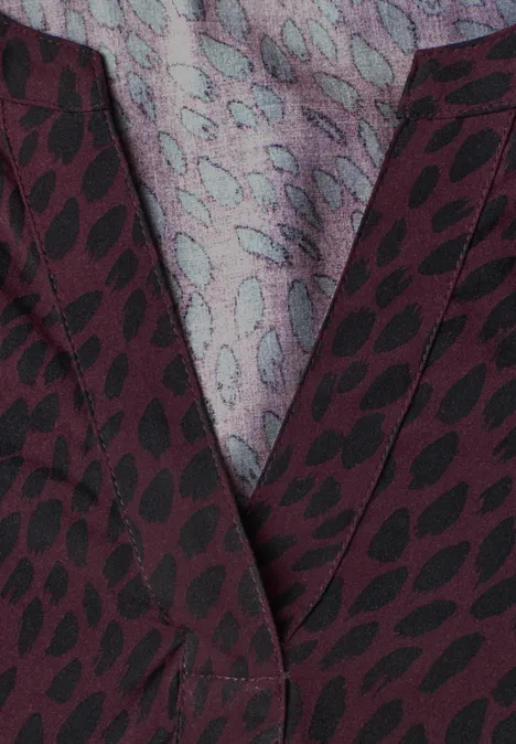 Nahaufnahme eines burgunderroten Stoffes mit schwarzem Blättermuster und hellblaugrauem Inneneinsatz.