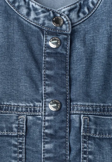 Naheansicht einer blauen Jeansjacke mit silbernen Druckknöpfen und zwei aufgesetzten Taschen.