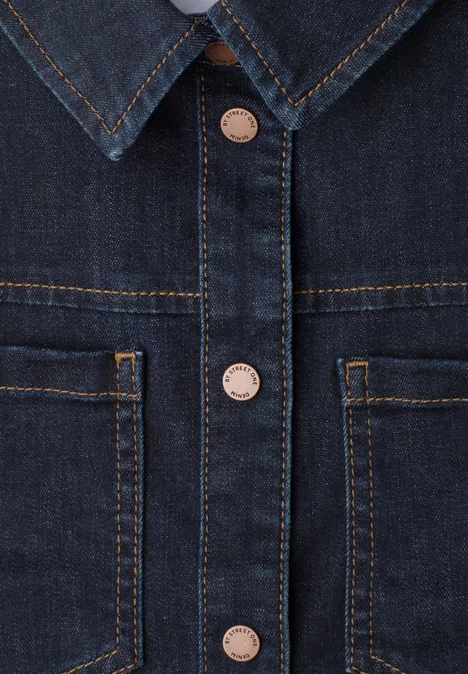 Nahaufnahme einer blauen Jeansjacke mit Kragen, Knopfleiste und aufgesetzten Taschen.