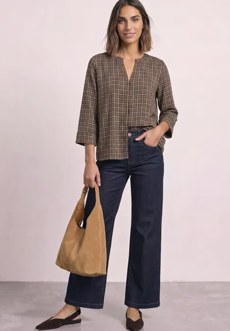 Dame in karierter brauner Bluse mit V-Ausschnitt, weiten Jeans und cognacfarbener Wildledertasche.