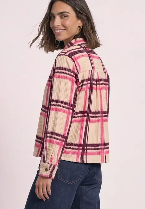 Frau in beige-rosa karierter Hemdjacke und Jeans blickt lächelnd über die Schulter.