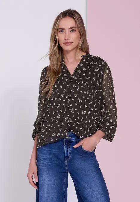 Vrouw in een donkerblouse met patroontjes en blauwe jeans voor een tweekleurige roze achtergrond.