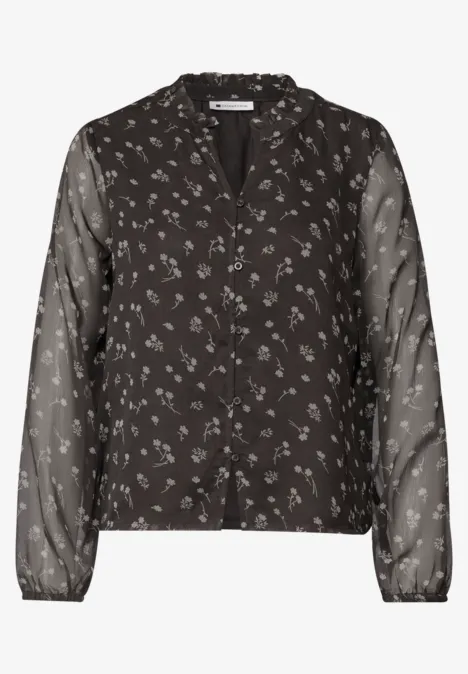 Zwarte blouse met knoopsluiting, klein wit bloemenprint en lange, transparante mouwen.