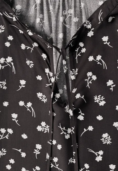 Schwarze Bluse mit weißem Blumenmuster und Bindeband am Ausschnitt.