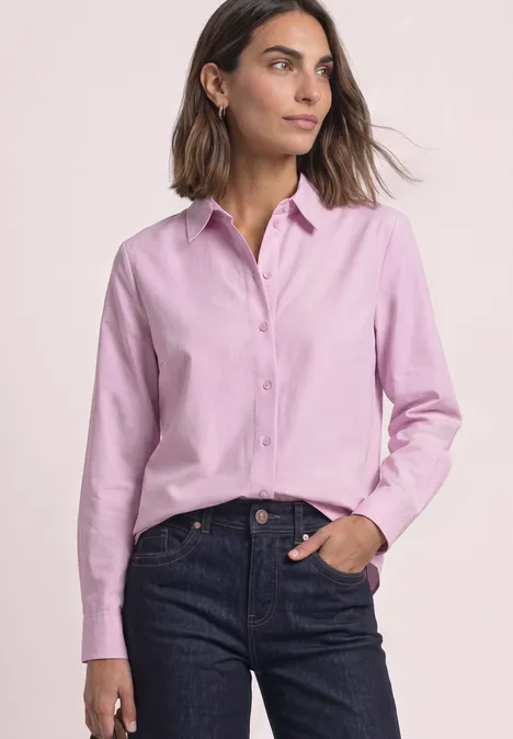 Chemisier Oxford avec imprimé dans le dos vintage blush Frau in pinker Hemdbluse und dunkler Jeans mit einer Hand in der Hosentasche.