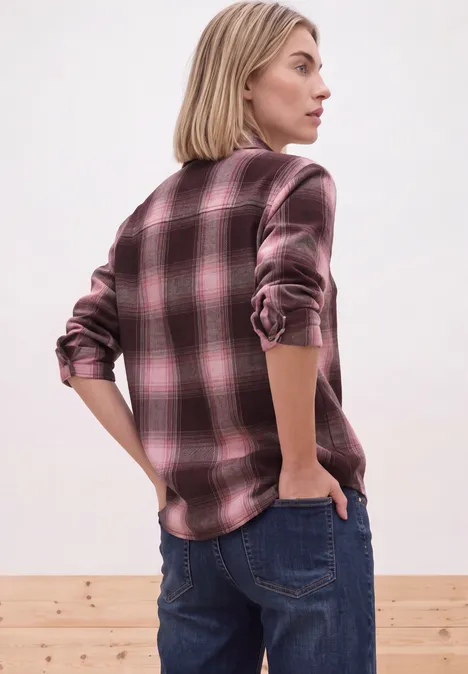 Frau von hinten in pink-schwarzem kariertem Hemd und blauen Jeans vor schlichtem Hintergrund.