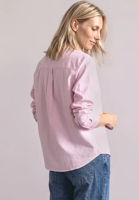 Eine Frau von hinten in einer rosafarbenen Bluse und Jeans vor hellem Hintergrund.