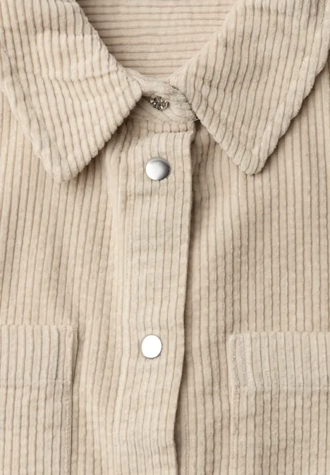 Close-up van voorkant van beige corduroy-overhemdjas met zilverkleurige drukknopen en opgezette zakken.