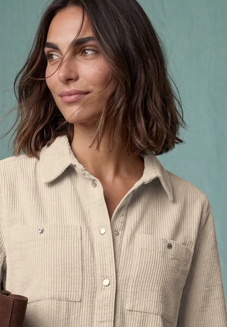 Portret van een glimlachende vrouw met halflang donker haar in een beige blouse voor een groene achtergrond.