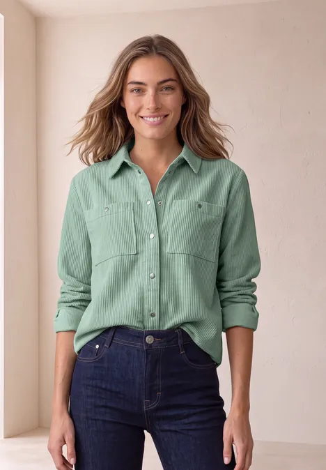 Overhemdblouse van corduroy met borstzakken eucalyptus green Eine lächelnde Frau trägt ein mintgrünes Hemd und blaue Jeans vor hellem Hintergrund.