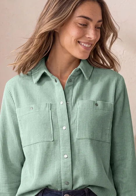 Overhemdblouse van corduroy met borstzakken eucalyptus green Eine lächelnde Frau trägt ein hellgrünes, langärmliges Hemd mit Brusttaschen.
