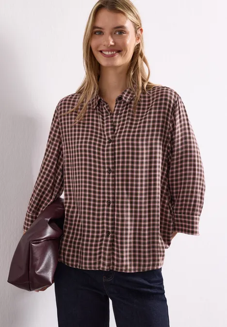 Bluzka z rękawami 3/4 w kratkę warm blush Uśmiechnięta kobieta ma na sobie kraciastą bluzkę, dżinsy i trzyma dużą skórzaną torbę.