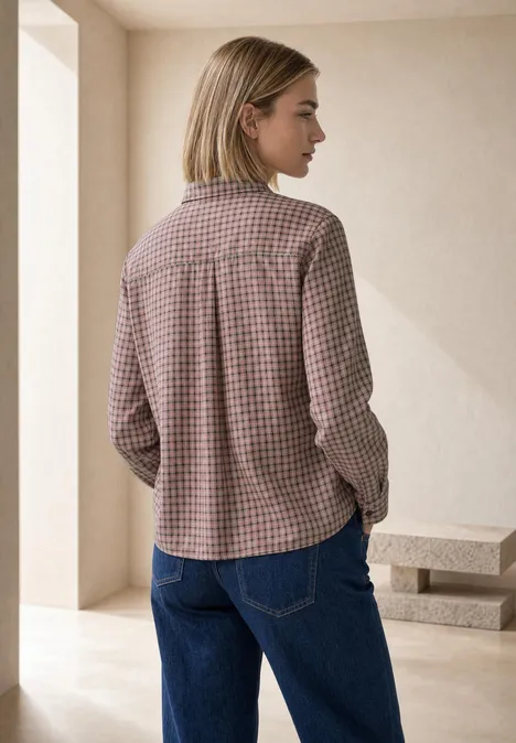 Frau von hinten in kariertem Hemd und blauen Jeans vor schlichter Wand.