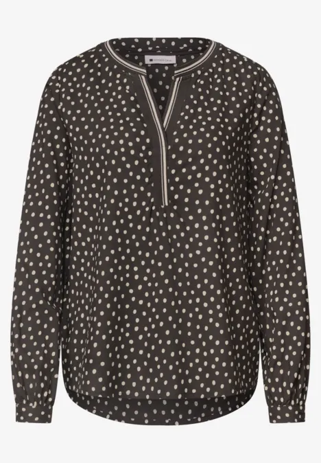 Schwarze Bluse mit cremefarbenen Tupfen, V-Ausschnitt, langen Ärmeln und abgerundetem Saum.