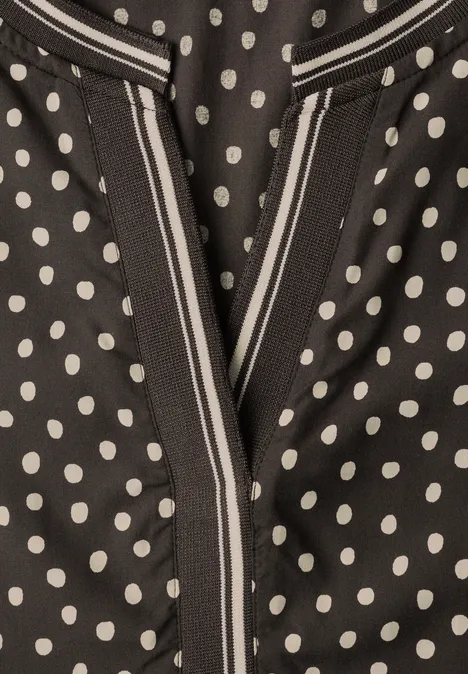 Schwarzes Kleidungsstück mit weißen Polka Dots und V-förmiger Nahtöffnung.