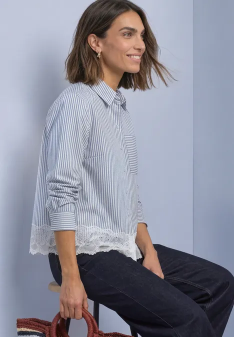 Chemisier à manches longues, rayé et orné d'une bordure en dentelle northern blue Frau mit halblangem Haar in blau-weiß gestreiftem Hemd mit Spitze sitzt seitlich auf einem Hocker.