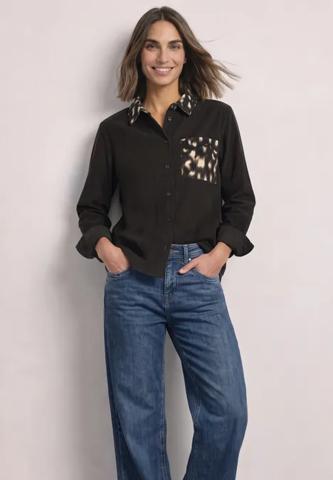 Chemisier à manches longues avec des détails imprimés représentant des chevreuils black coffee Frau in schwarzem Hemd mit gemustertem Kragen und Tasche sowie blauen Jeans, lächelnd