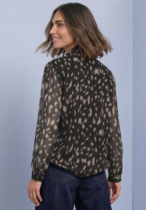 Chemisier à manches longues en chiffon avec nœud décoratif Black Frau in gemusterter, schwarz-beiger Bluse und dunkler Jeans schaut über die Schulter.